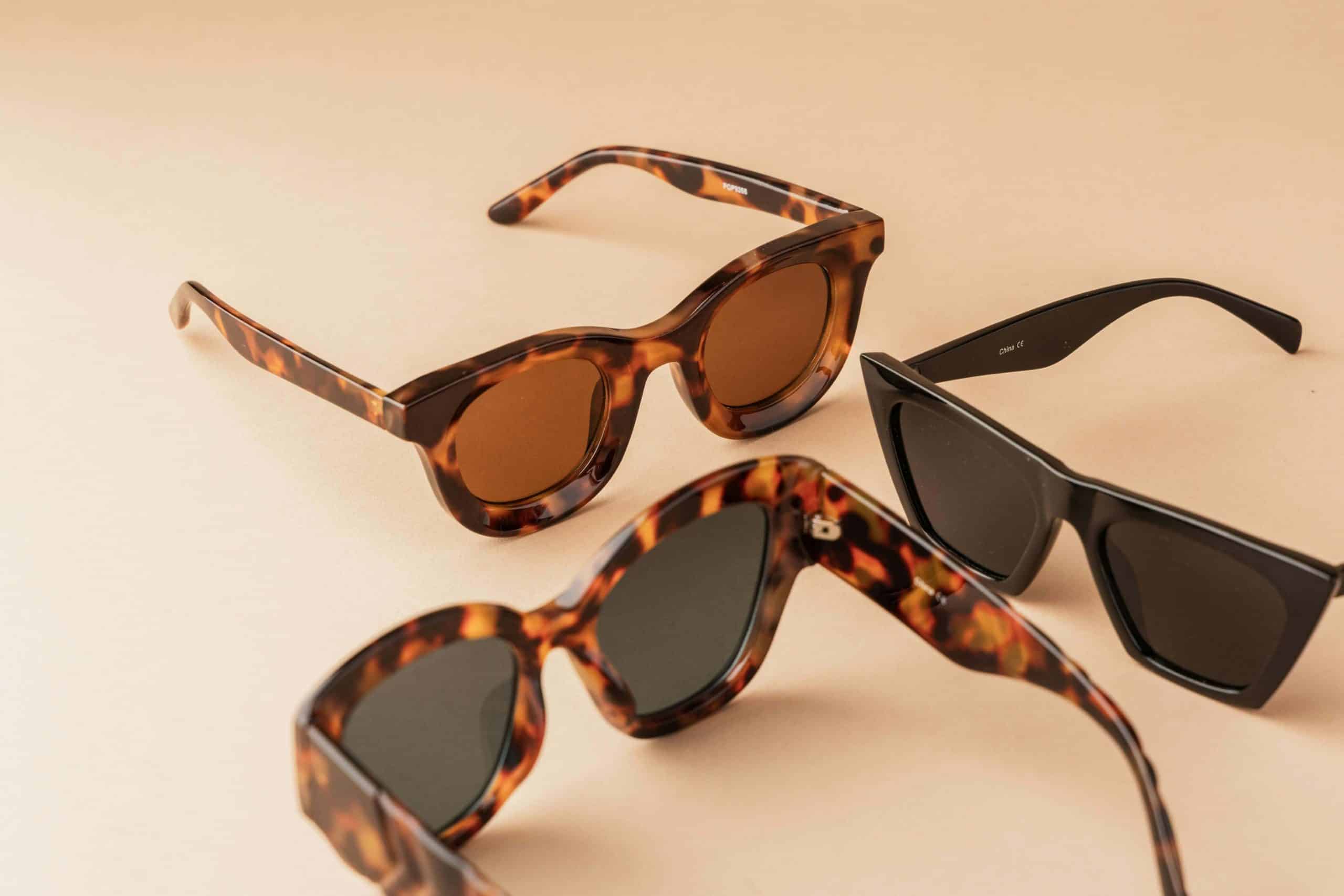 Three pairs of sunglasses, two with tortoiseshell frames, on a pale orange background.